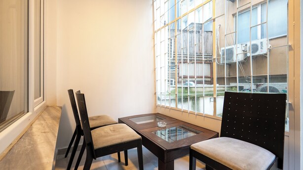 A corner room with a glass-top table, two chairs, and a large window overlooking a building with air conditioning units. - Charming 3-Bedroom Apartment in the Heart of Kadıköy (Kadıköy)