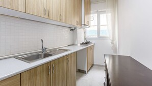 A kitchen with wooden cabinets, a white countertop, a stainless steel sink, and a window with white curtains. - Charming 3-Bedroom Apartment in the Heart of Kadıköy (Kadıköy)