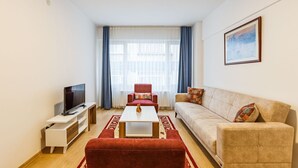 A modern living room with a flat-screen TV, a red sofa, a beige sofa, and a coffee table. - Charming 3-Bedroom Apartment in the Heart of Kadıköy (Kadıköy)