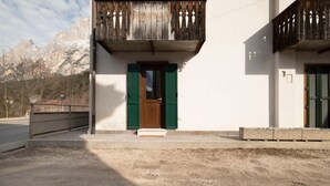 Un edificio con balcón de madera, una puerta con contraventanas verdes y montañas al fondo.