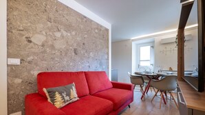 Un sofá rojo con un cojín decorativo, una zona de comedor con una mesa y sillas, y una cocina con mostrador y armarios.
