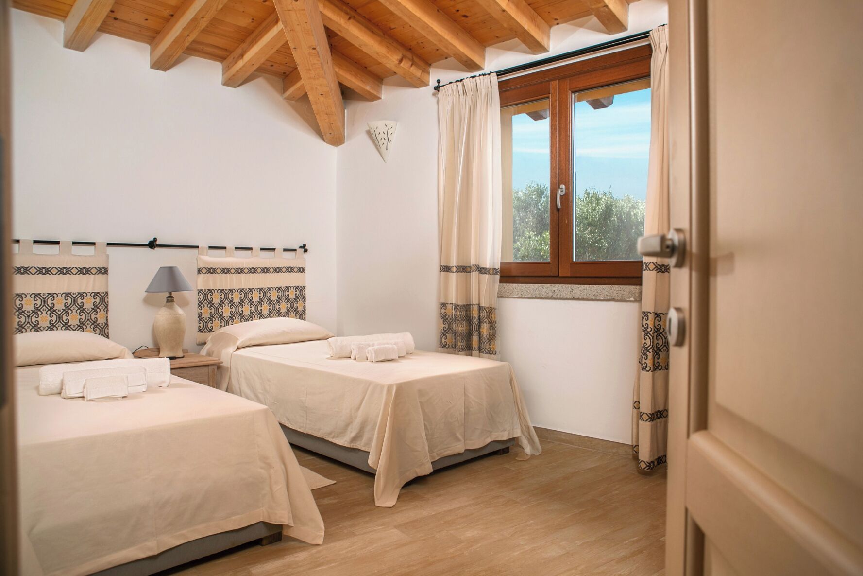 Una camera da letto con due letti, una finestra con tende e un soffitto in legno.
