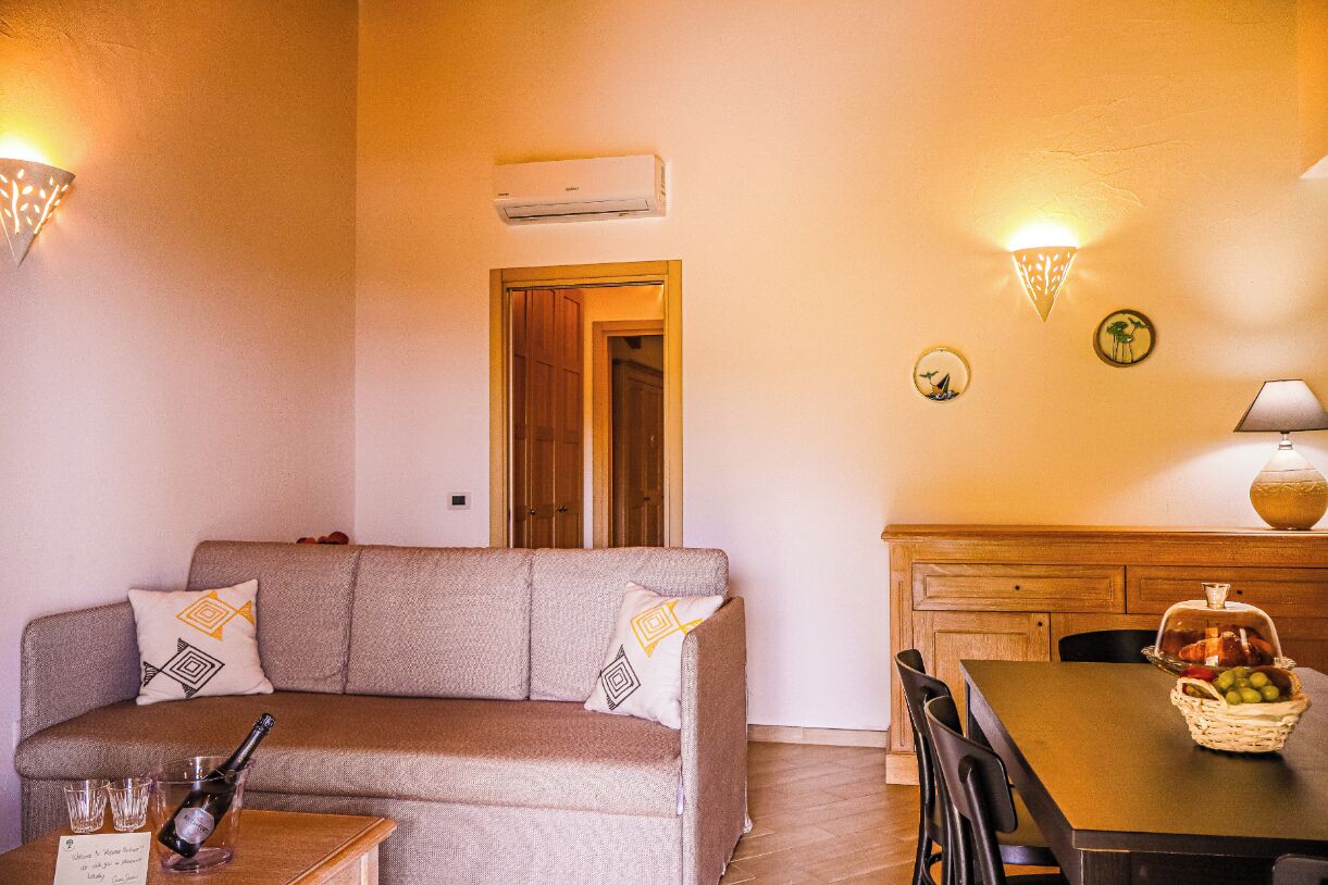 Una sala de estar acogedora con un sofá, una mesa de comedor con una cesta de fruta y un aire acondicionado de pared.