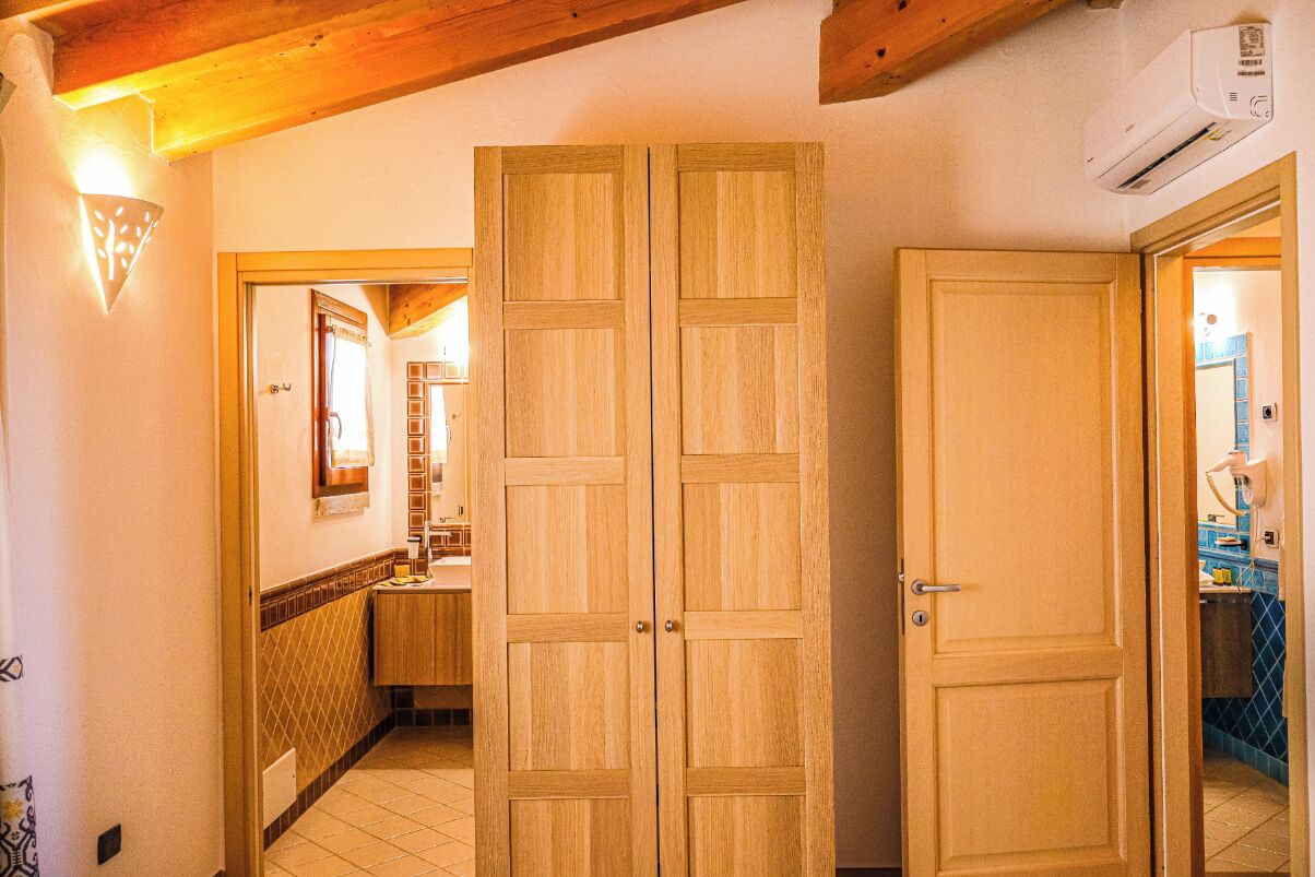 Un pasillo con puertas dobles de madera, suelo de baldosas y una cocina visible a través de un vano abierto.