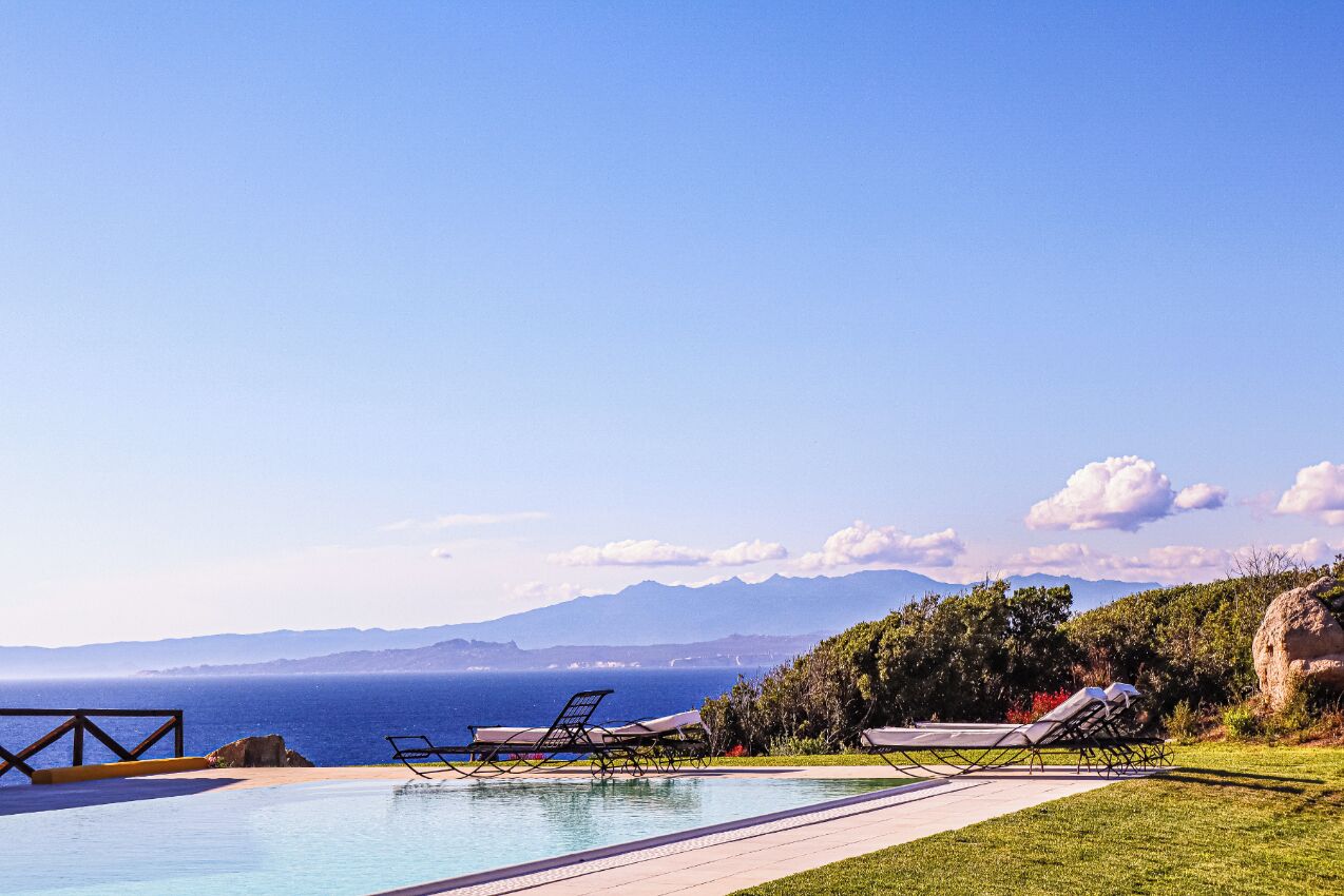 A poolside area with lounge chairs and a view of the sea and mountains.