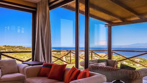 A room with a large window overlooking a coastal landscape, furnished with a sofa, chairs, and a small table.