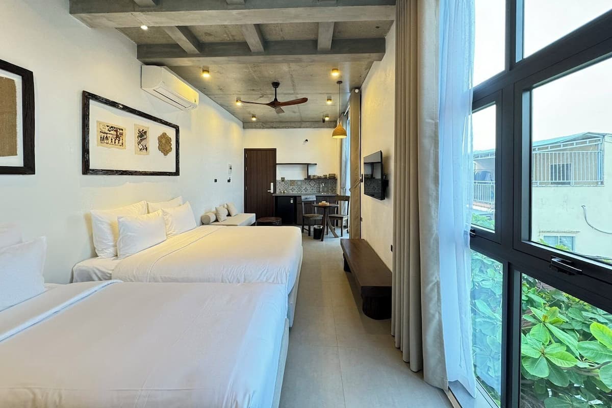 Habitación de hotel con dos camas, kitchenette, comedor y ventanas amplias con vistas.