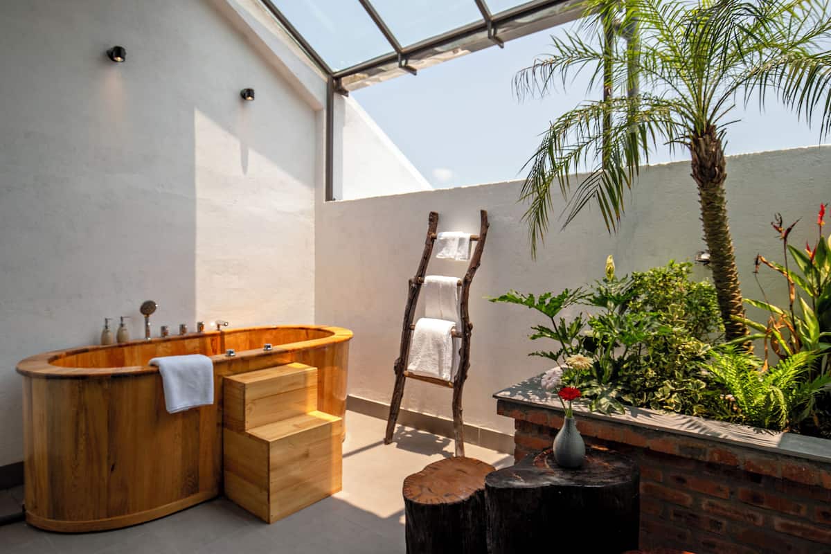 Un baño moderno con una bañera de madera, una escalera de madera y un pequeño rincón con plantas.