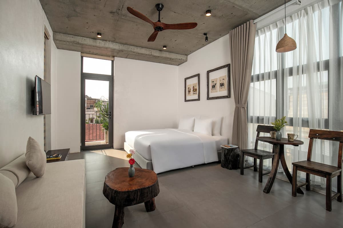 Una habitación de hotel moderna con una cama grande, un sofá, una mesa de centro de madera y un comedor con sillas y una mesa.