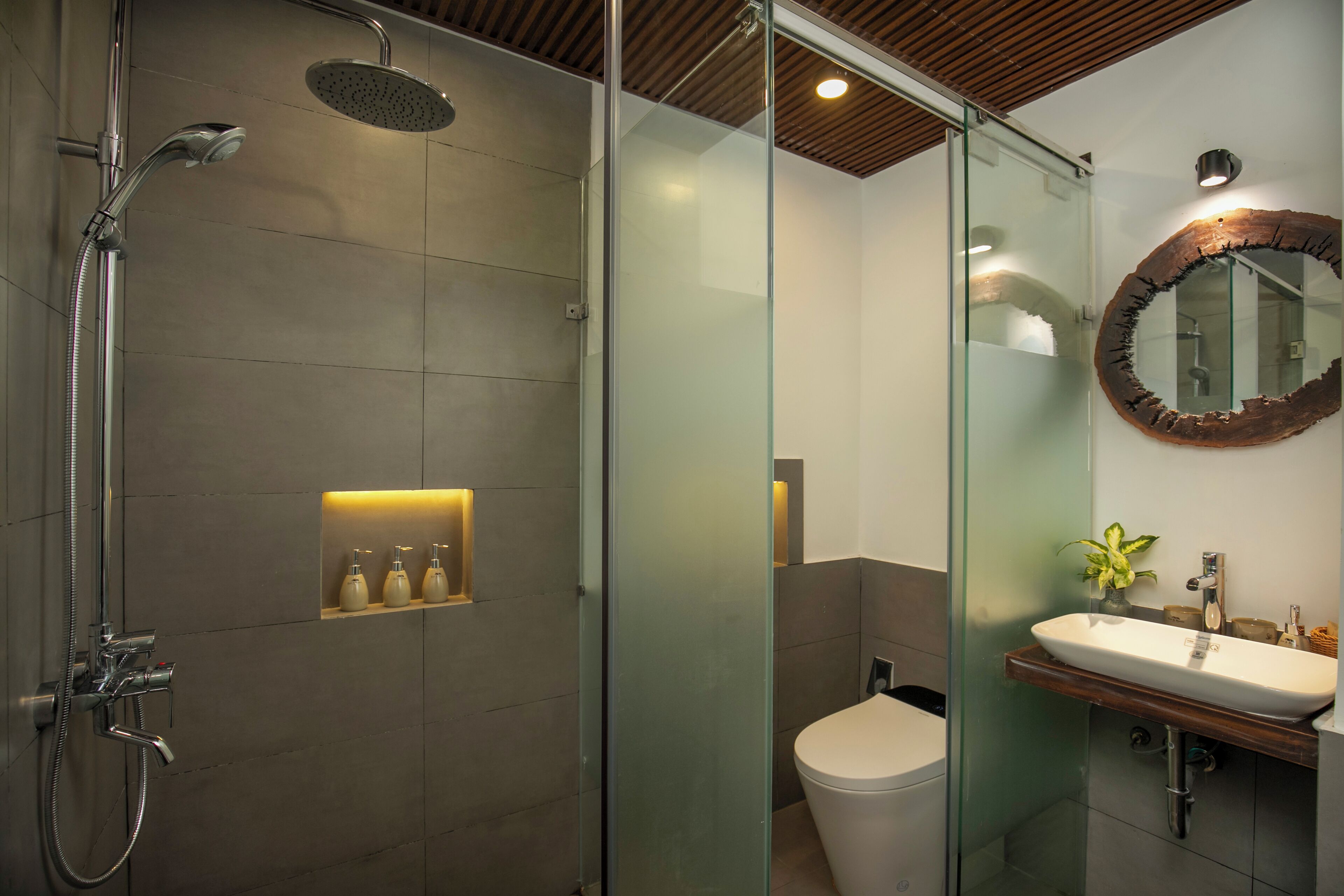 A modern bathroom with a glass-enclosed shower, a wooden vanity, and a round mirror with a rustic frame.