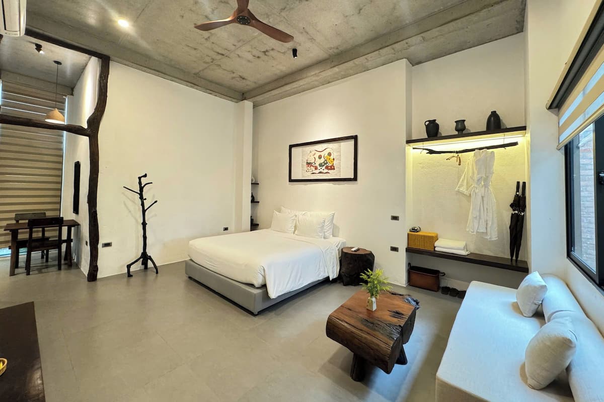 Un dormitorio moderno con cama, mesita de noche y una zona de estar con sofá.