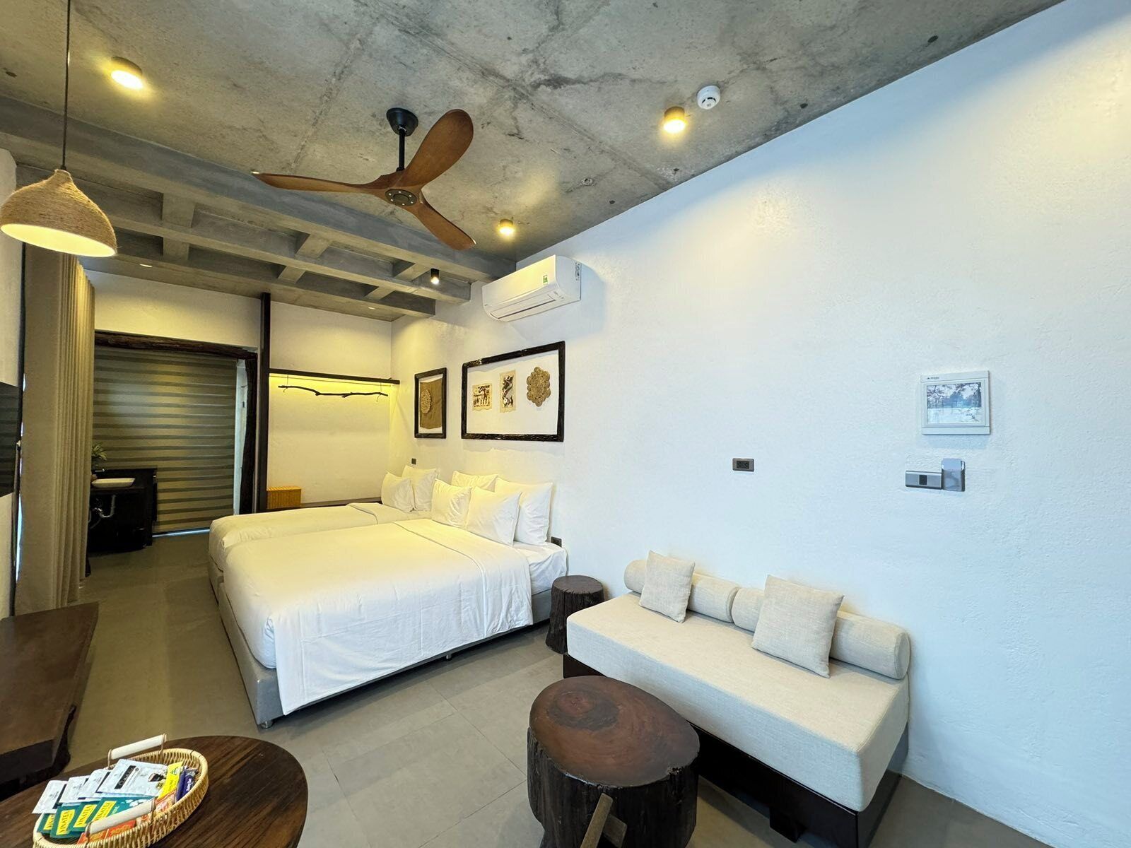 A modern hotel room with a large bed, a sofa, a dining table, and a ceiling fan.
