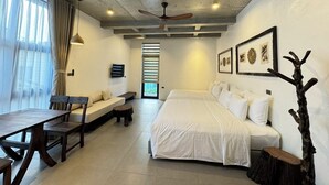 A modern bedroom with a large bed, a desk, and a chair. There is a ceiling fan, a window with curtains, and a door leading to another room. - Eco & Rustic Home Hoian (Da Nang)