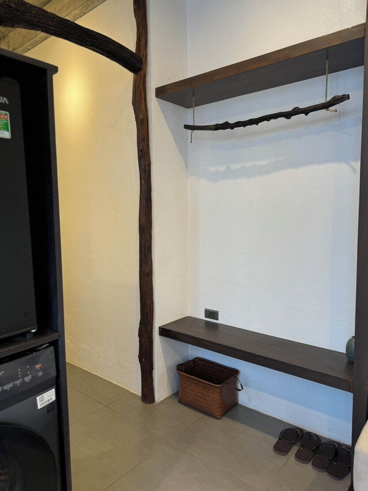 A room with a black cabinet, a wooden beam, a shelf with a branch, a basket, and a pair of shoes.