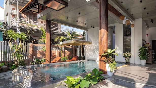 A swimming pool with a stone border, surrounded by potted plants and a wooden deck. - Eco & Rustic Home Hoian (Da Nang)