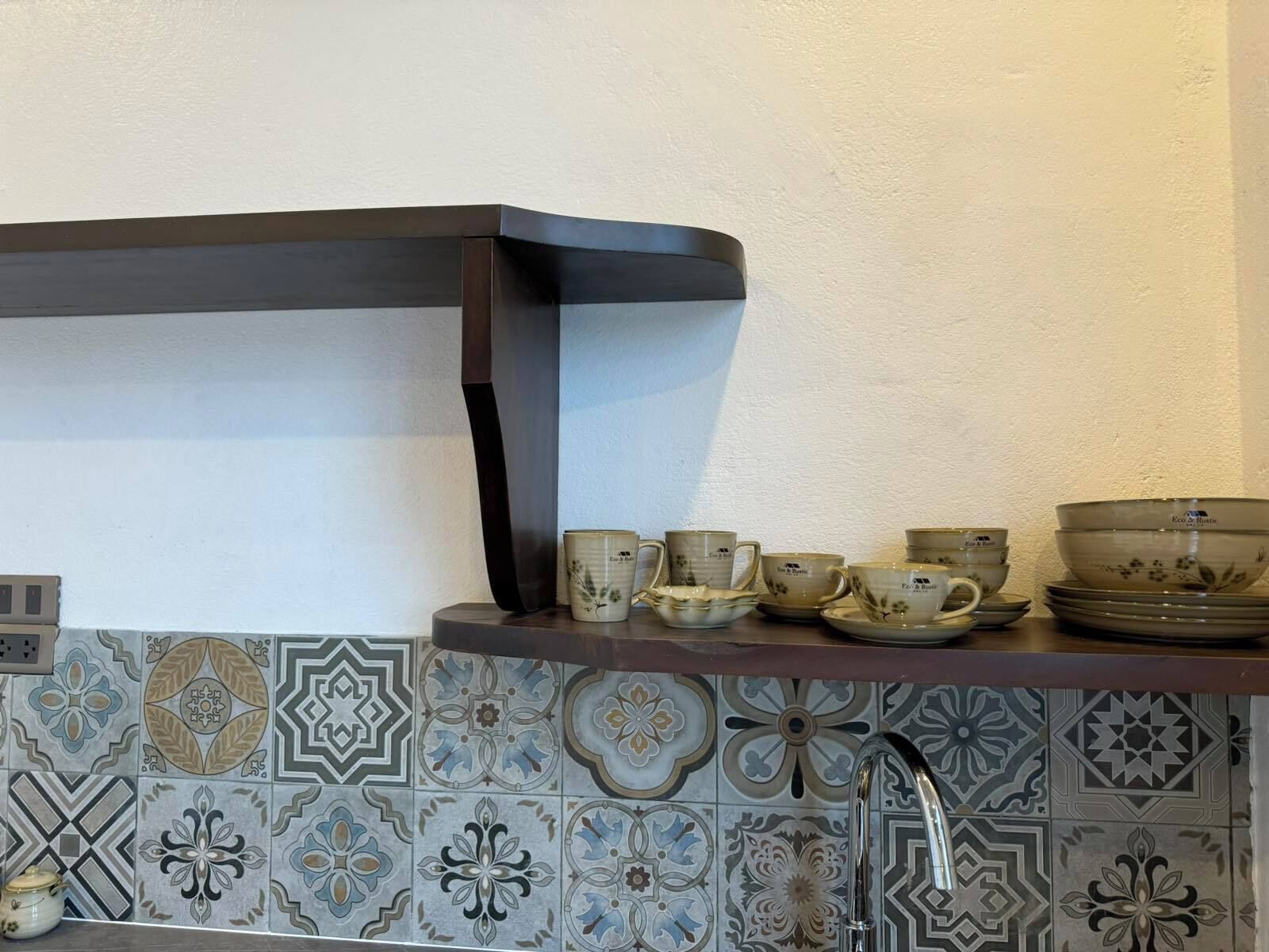 A kitchen with a dark wooden shelf holding various ceramic cups and saucers.