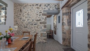 Un comedor con pared de piedra, mesa de madera, sillas y una puerta blanca con ventanal.