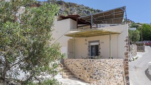 Un edificio de paredes de piedra con un balcón y una escalera que conduce a la entrada, con vistas a una colina.