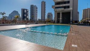 A swimming pool with clear water, surrounded by a wooden deck and a cityscape in the background.