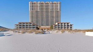 Un hotel grande con varios pisos y balcones, ubicado en una playa de arena con cielos despejados.