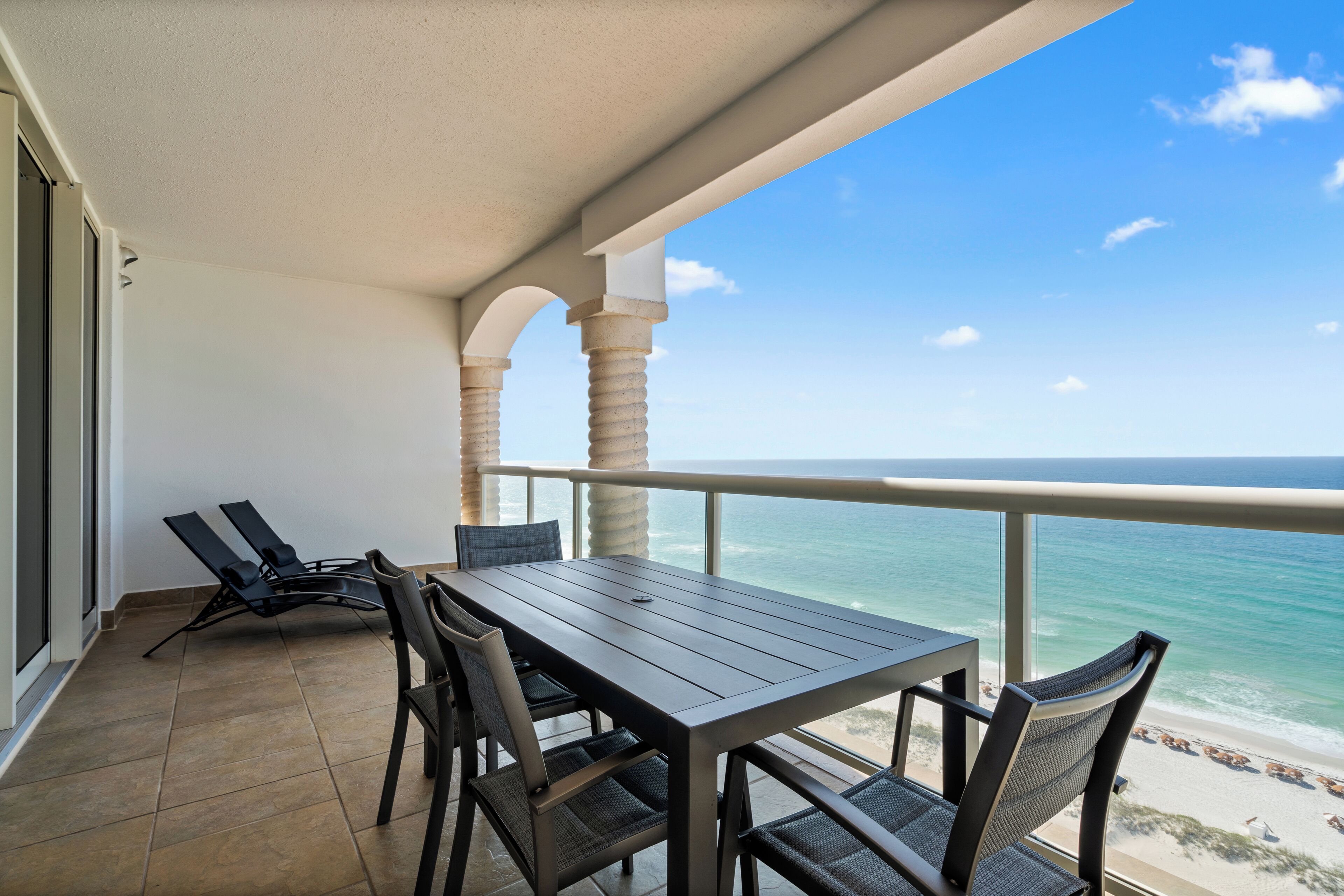 A balcony with a table and chairs, overlooking a beach and ocean.