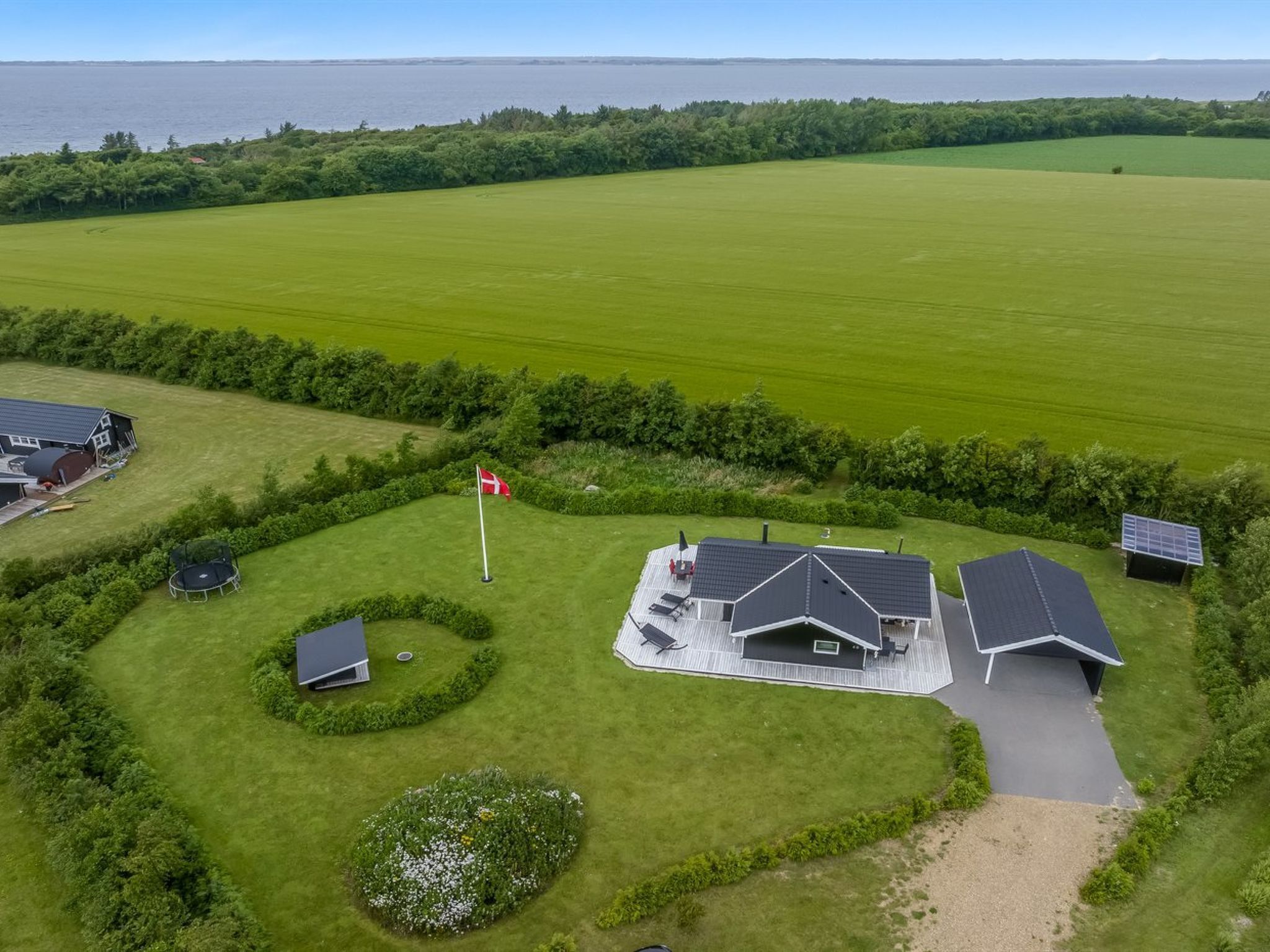 Luchtbeeld van een woonhuis met een groot groen veld, een huis met schuin dak, zonnepanelen en een vlag.