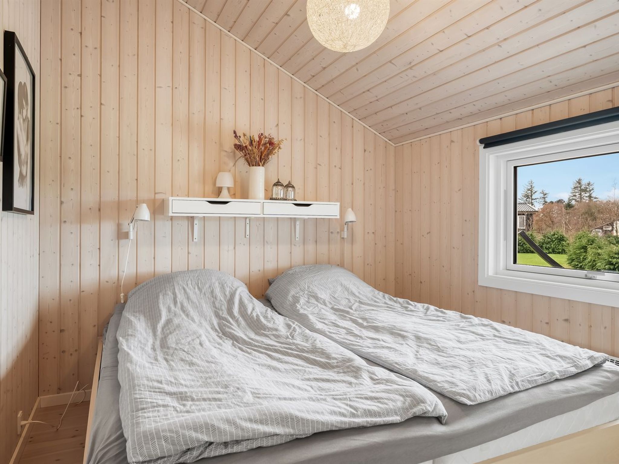 Een slaapkamer met een bed, een raam en een houten wand.