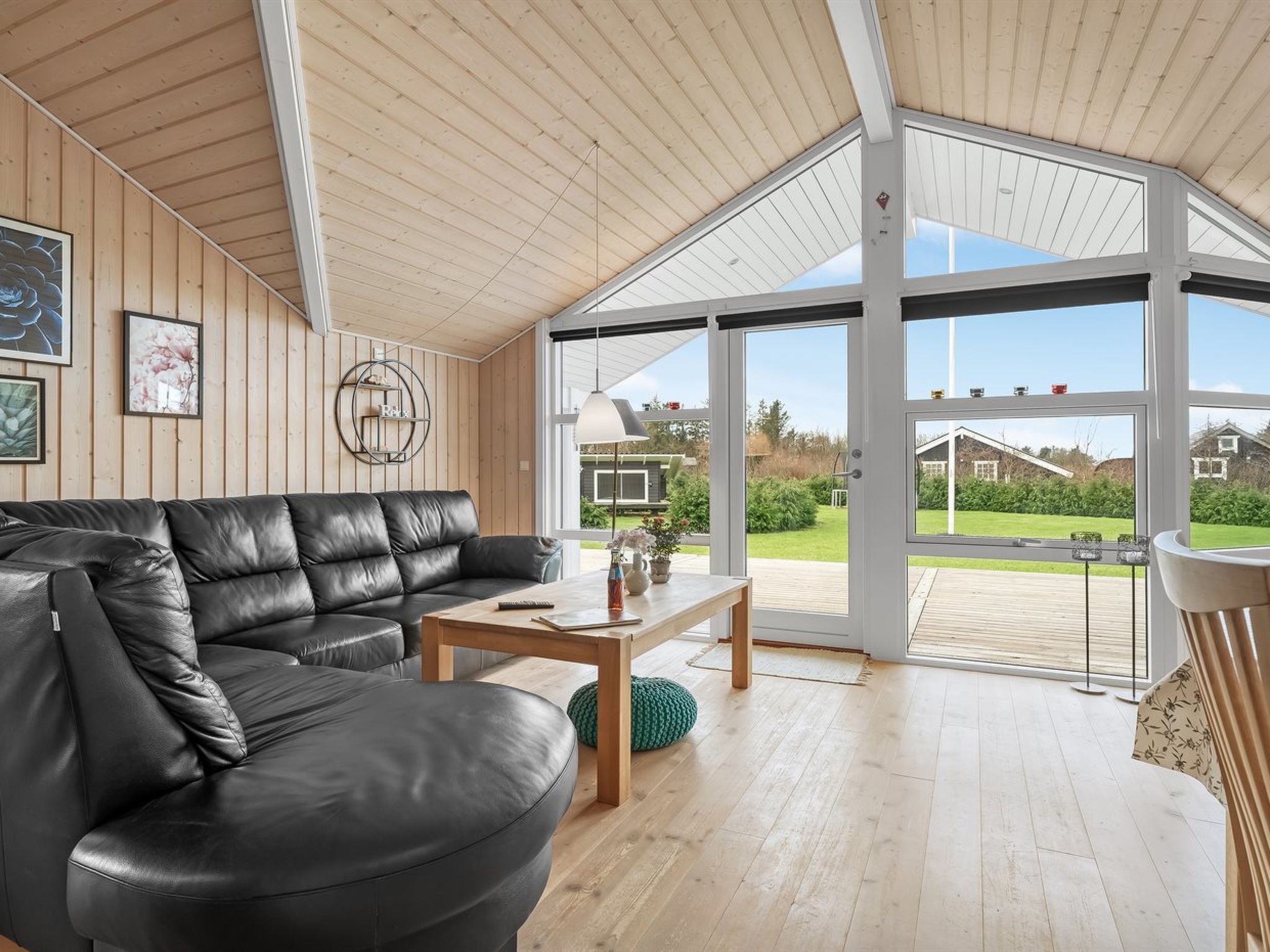 Un salon moderne avec un canapé en cuir noir, une table basse en bois et une grande porte vitrée donnant sur une terrasse.