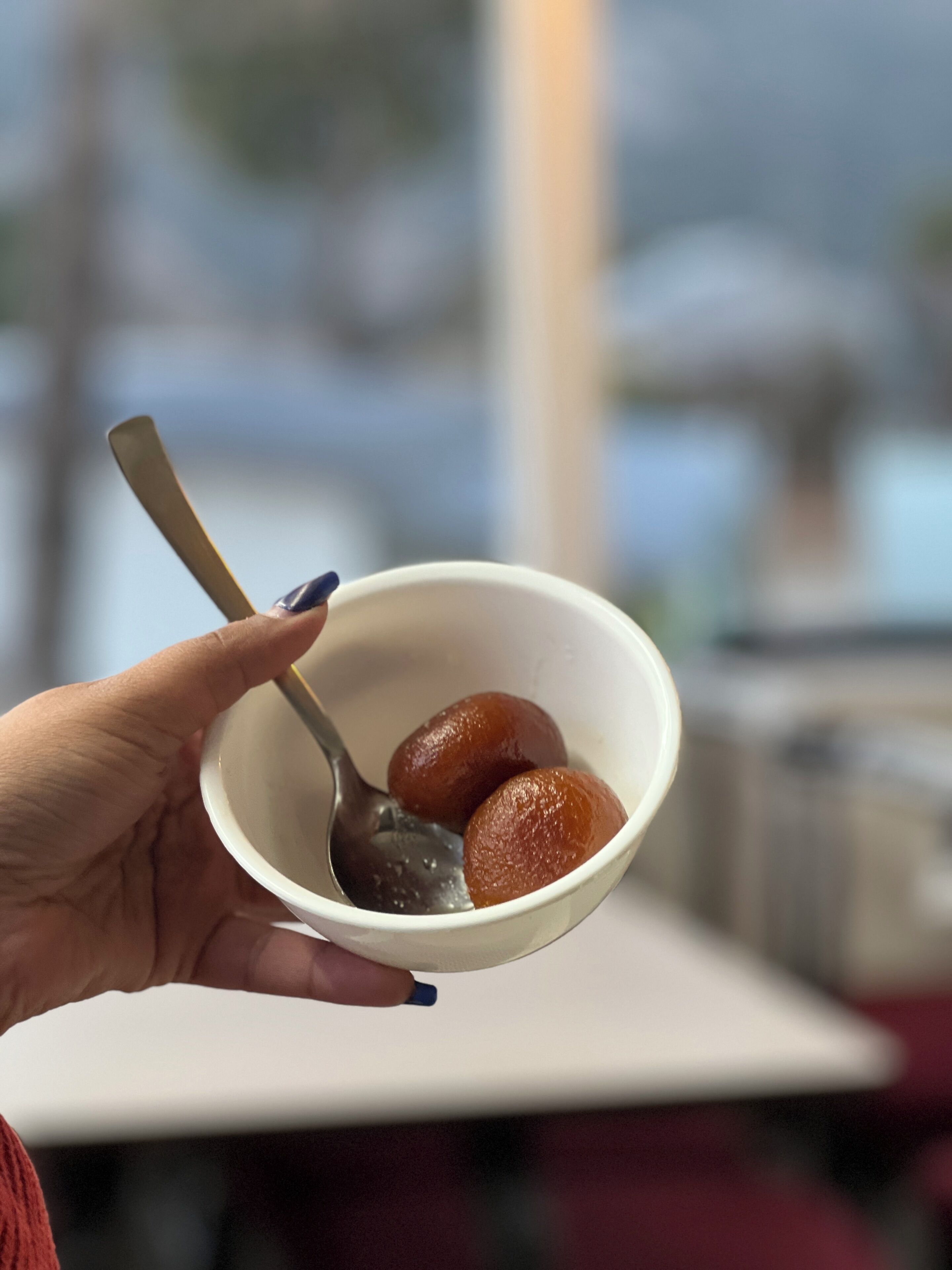 A hand holding a bowl with two round, brown sweets and a spoon.