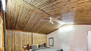 A bedroom with a sloped ceiling, wooden flooring, a bed, a bedside table, a lamp, a chair, and a rug. - THE CHAIL HEIGHTS HOTEL&RESORT (Shimla)