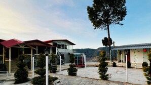 A building with a stone facade, a red roof, and a staircase leading to a second floor. There are trees and a clear sky in the background. - THE CHAIL HEIGHTS HOTEL&RESORT (Shimla)