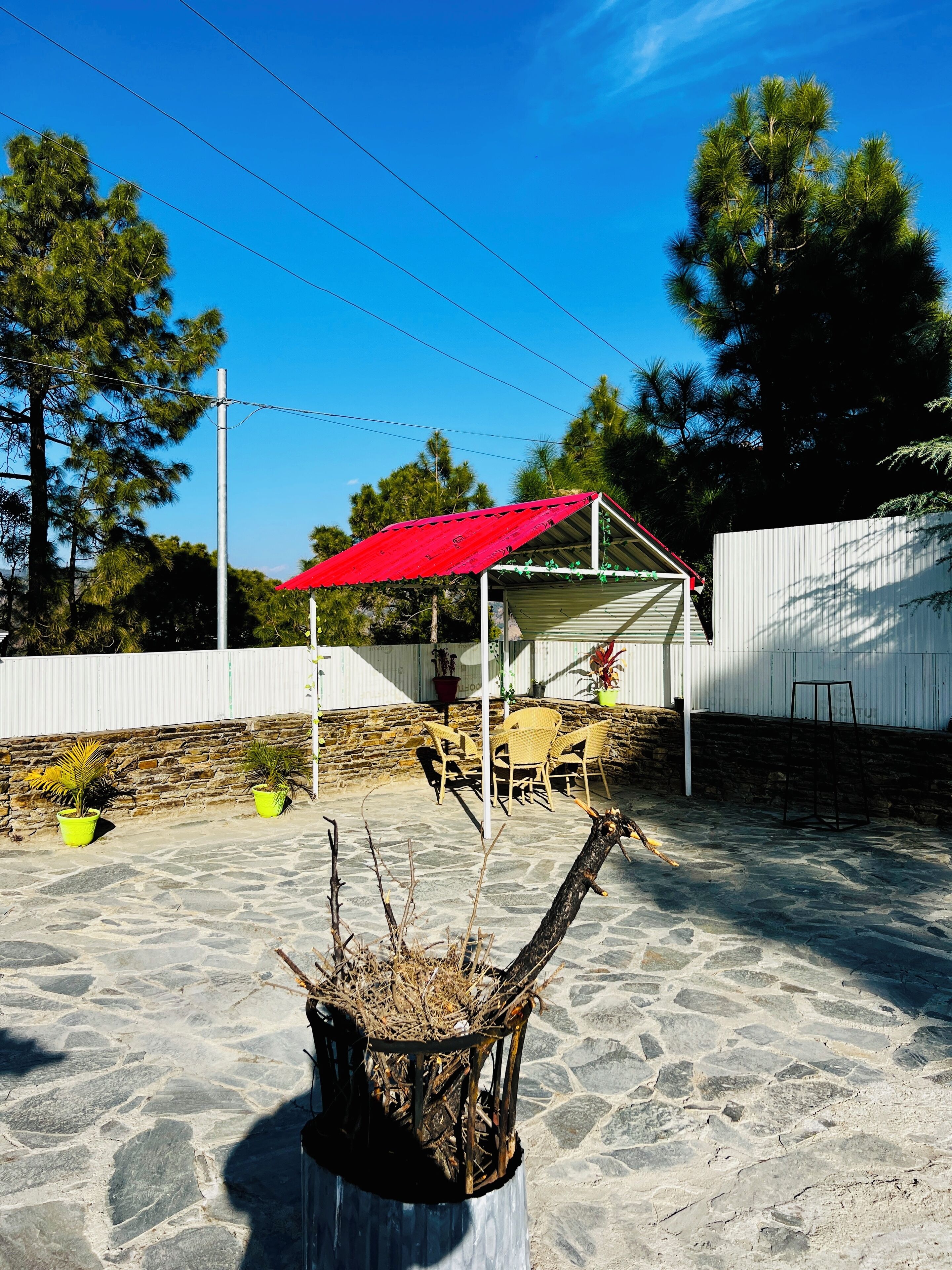 A patio area with a stone floor, a red umbrella, wicker furniture, and potted plants.