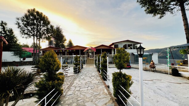 A stone pathway leading to a building with a red roof, surrounded by trees and a view of a mountainous landscape. - THE CHAIL HEIGHTS HOTEL&RESORT (Shimla)