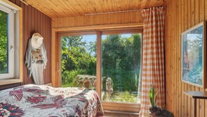 Ett rum med en säng, ett fönster med en gardin, en krukväxt och en hatt som hänger på väggen.