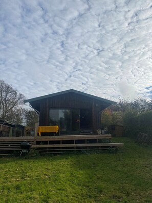 A wooden cabin with a large window, a deck, and a grill. - Romantic retreat close to the beach (Fårevejle)