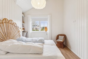 Une chambre à coucher avec un lit, une chaise en osier, une fenêtre et une étagère remplie de livres.