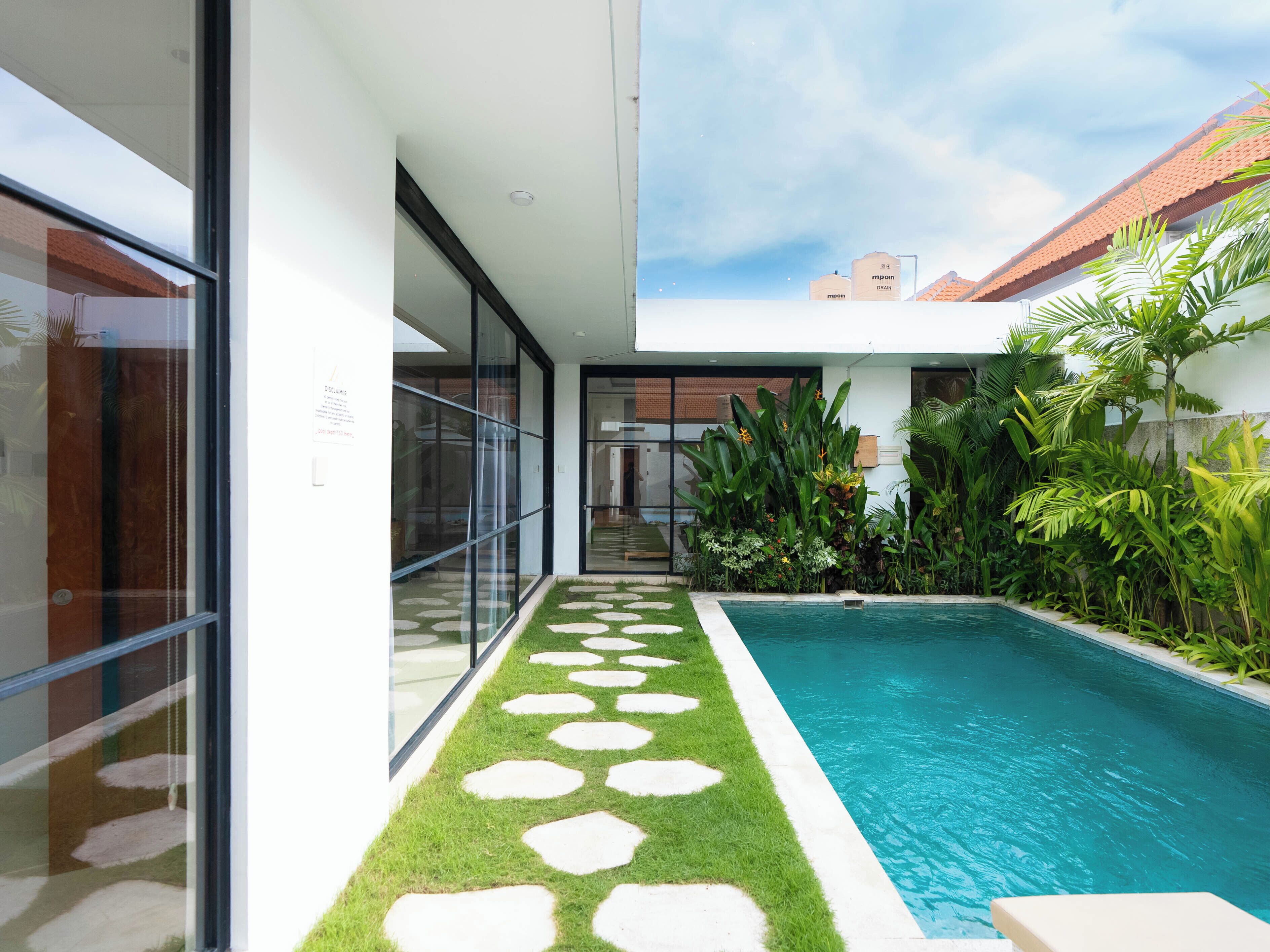 Una casa moderna con piscina, vetrate e un giardino con piante tropicali.