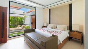 Una habitación de hotel moderna con una cama grande, un sofá, una mesita de noche y vistas a un jardín a través de una puerta de cristal.