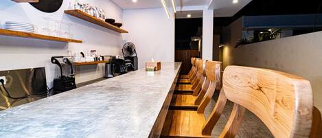 Un interior de café moderno con una larga barra de mármol, sillas de madera y un cartel que dice "LE CAFÉ".