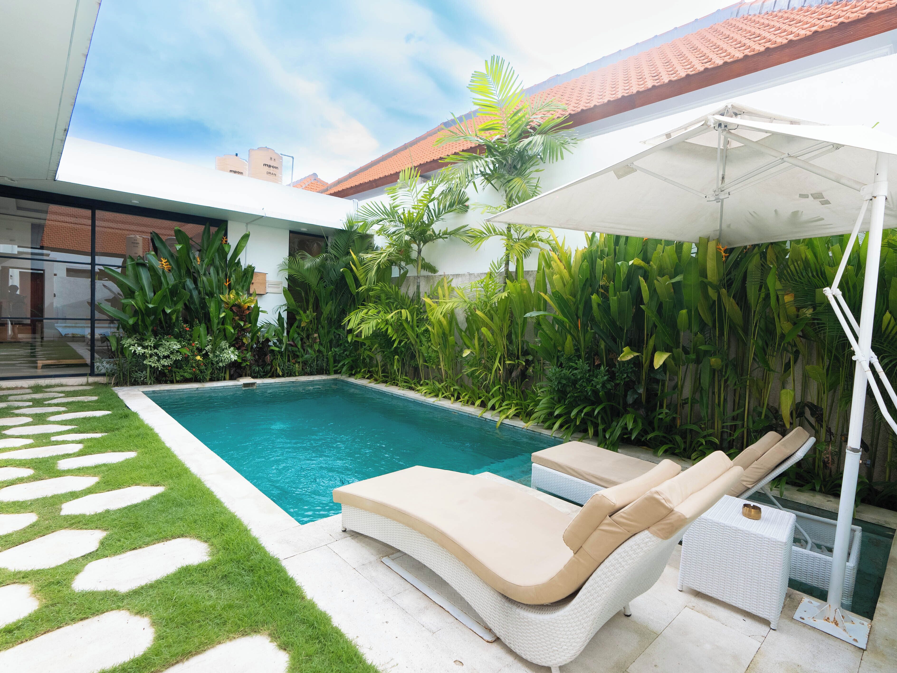A swimming pool with lounge chairs and a covered area, surrounded by lush greenery and a tiled roof.