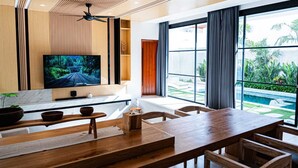 Un salón moderno con un televisor grande, muebles de madera y vistas a un jardín y piscina.