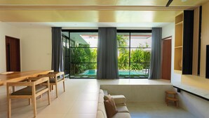 Una sala de estar moderna con una mesa de comedor de madera, un sofá color beige y vistas a un jardín a través de grandes ventanales.