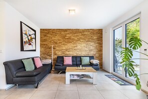 A modern living room with a black sofa, a wooden coffee table, and a brick wall. - House with 4 Bedrooms, Shared Terrace, Garden & Wi-Fi in Solingen (Solingen)