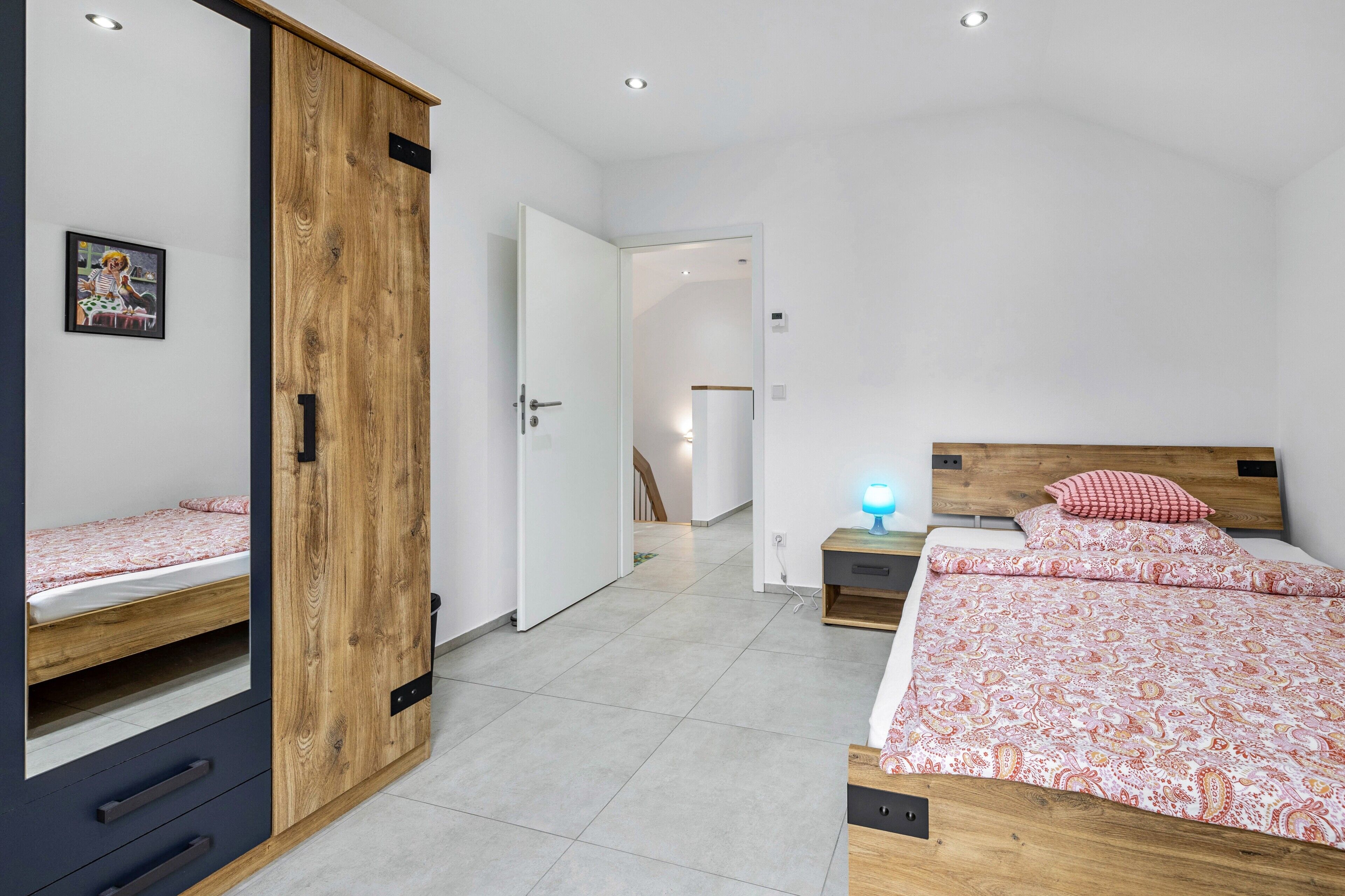 Une chambre à coucher comprenant un lit, une armoire, une table de chevet et une étagère fixée au mur.