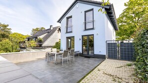 Una casa moderna con un patio, un comedor y un jardín cercado.