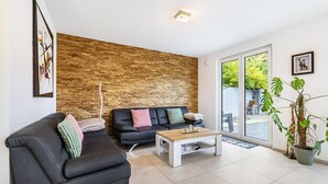 Una sala de estar moderna con un sofá de cuero negro, una pared de madera, una mesa de centro y una planta en maceta.