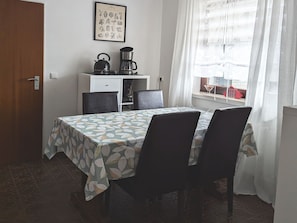 Un coin repas avec une table dressée pour quatre personnes, une machine à café et une estampe botanique encadrée au mur.
