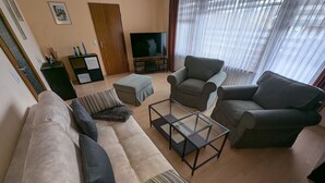 A living room with a sofa, two armchairs, a coffee table, a TV, and a door. - Apartment 'Buedinger Weg' with Wi-Fi (Gründau)