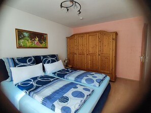 A bedroom with a bed, a wooden wardrobe, a painting on the wall, and a chandelier.