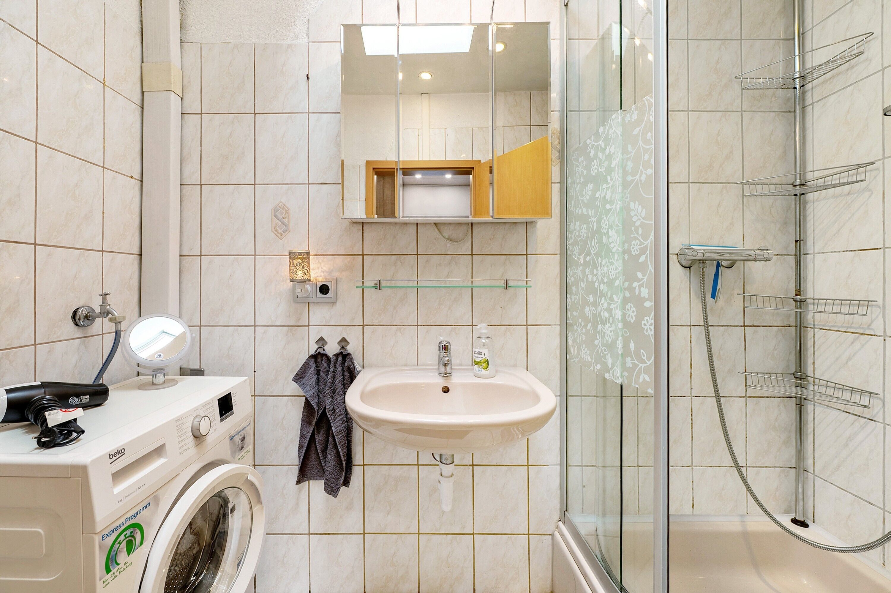 A bathroom with a washing machine, a sink, a mirror, and a shower.